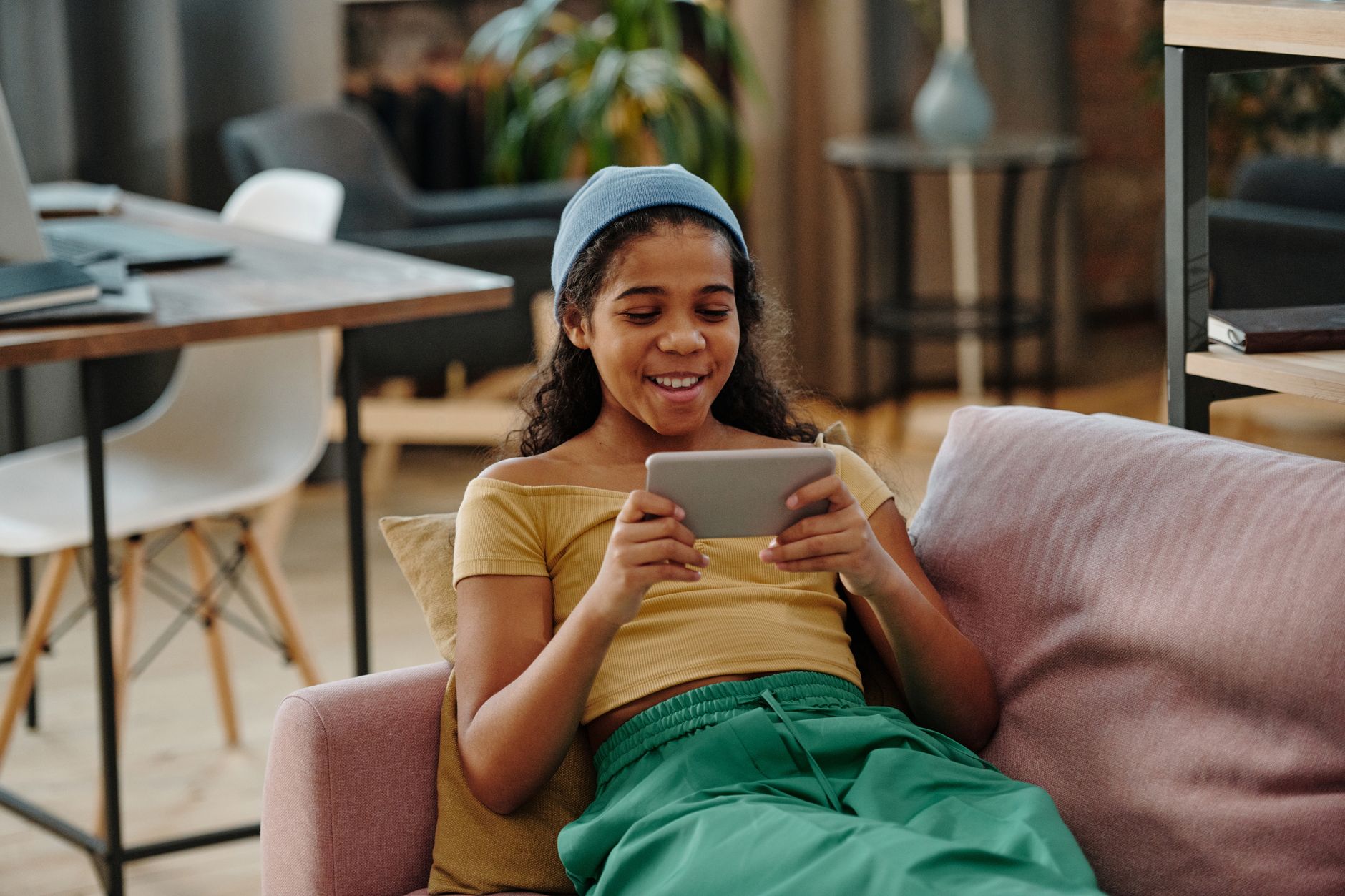 A young girl smiles while using a tablet on a cozy sofa in a modern living room.