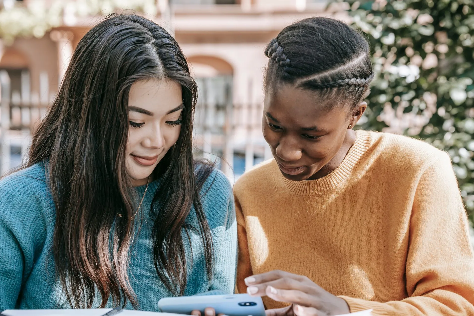 Cheerful young multiracial friends using mobile phone while watching video on blurred background of street