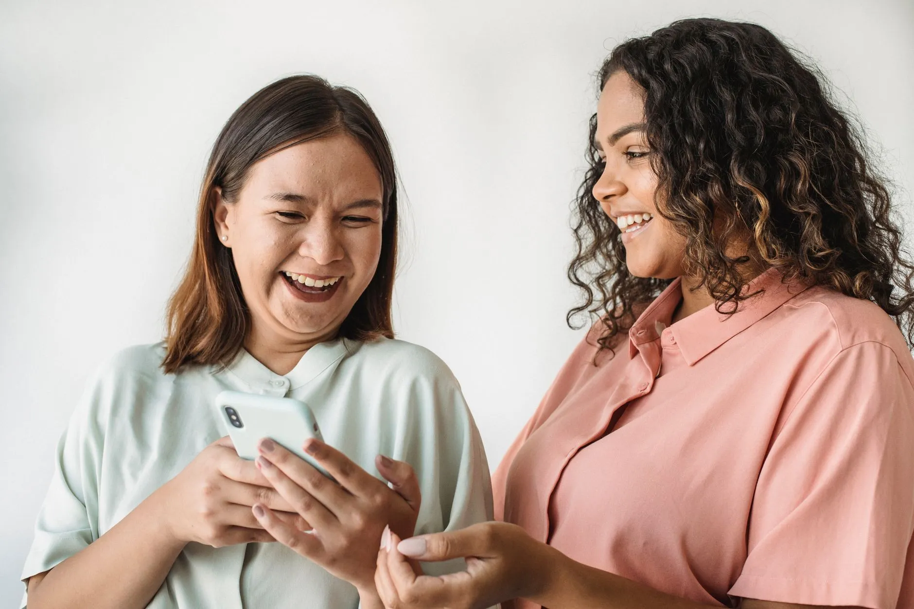 Two diverse women happily looking at and sharing something on a smartphone indoors.