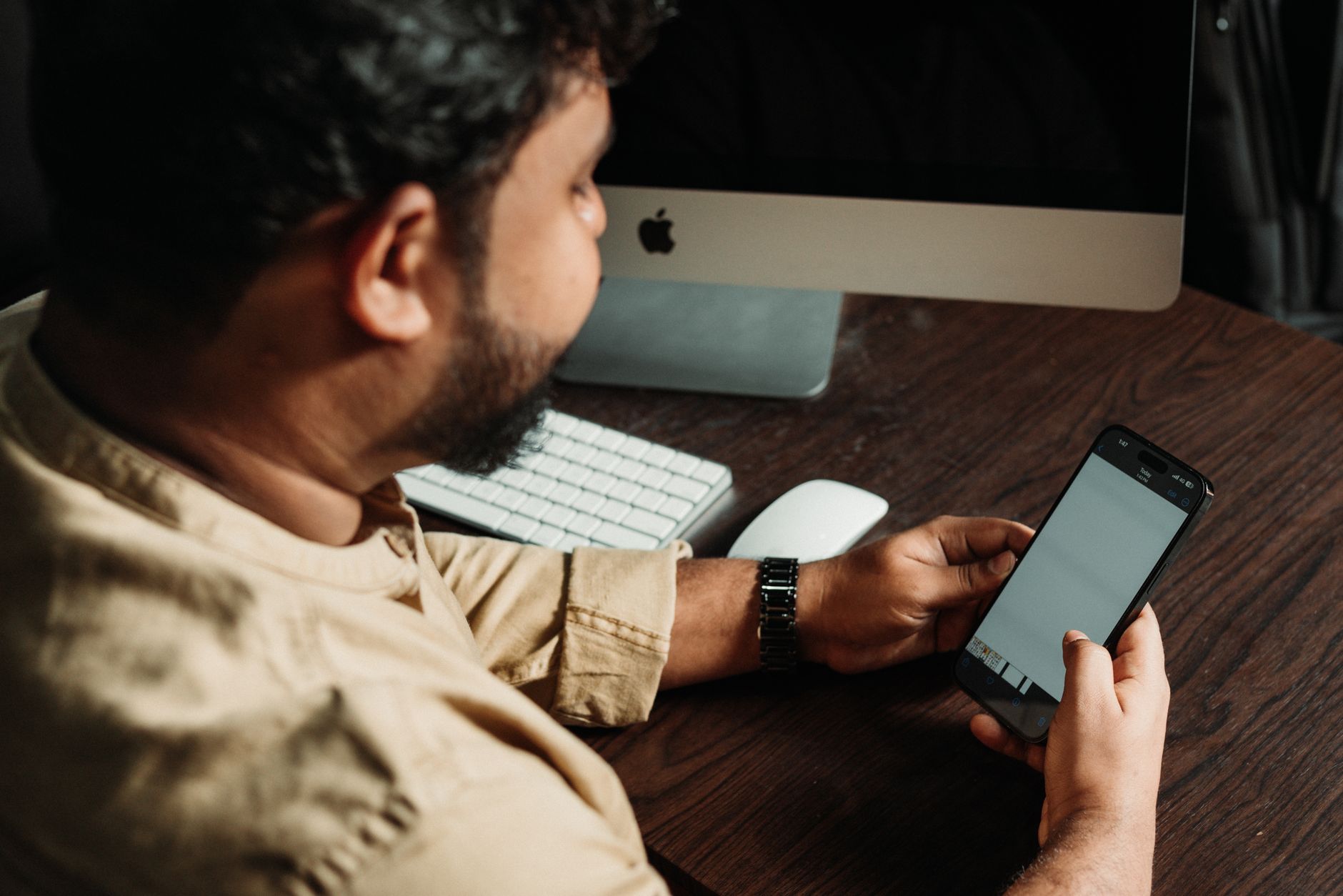 Man working on smartphone at office desk with computer, illustrating technology in business.