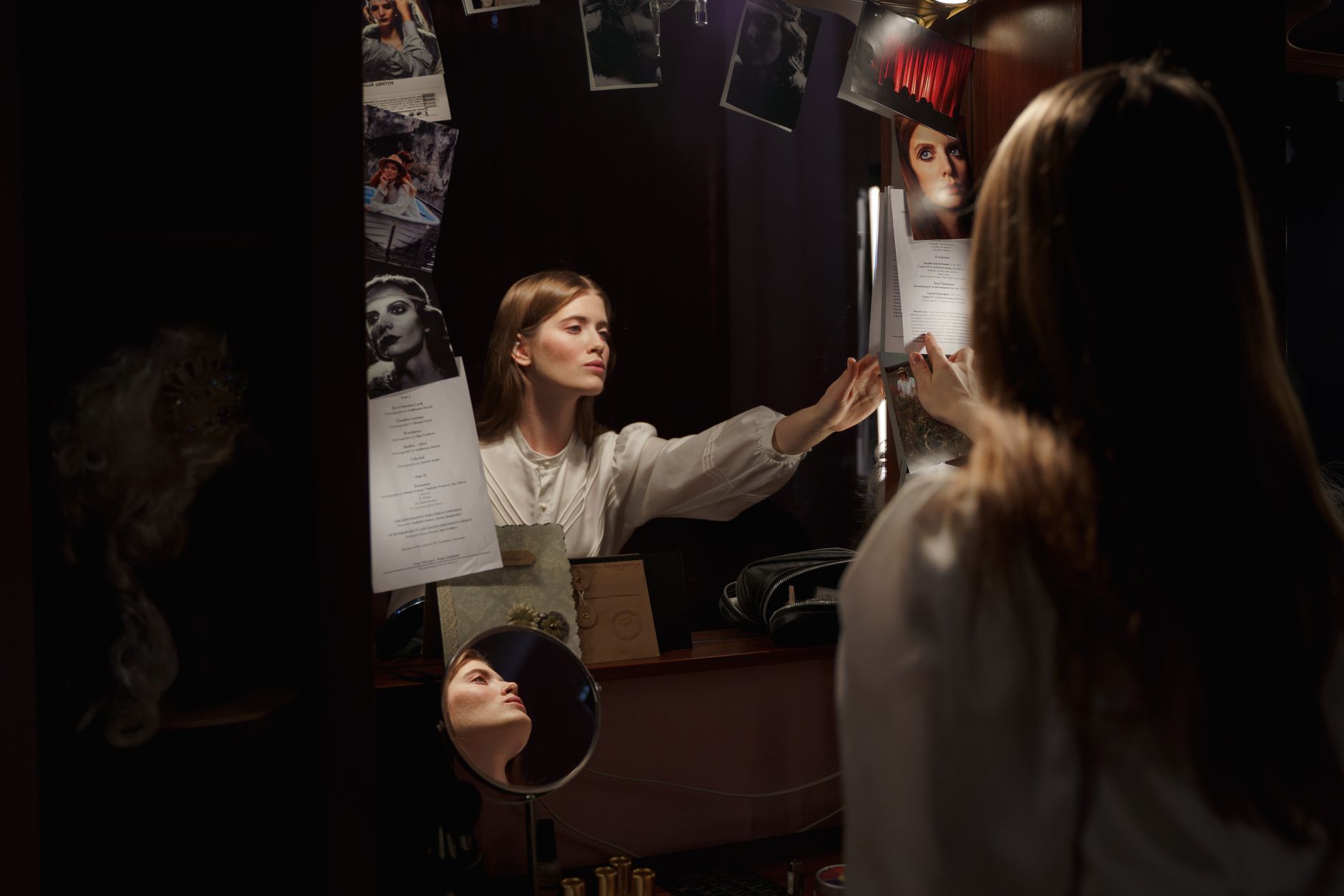 An actress adjusts her script in front of the dressing room mirror, preparing for her performance.