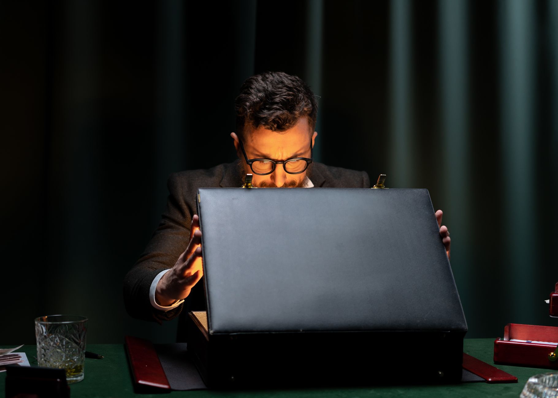 A man in a black suit is intriguingly opening a briefcase in a dimly lit room.