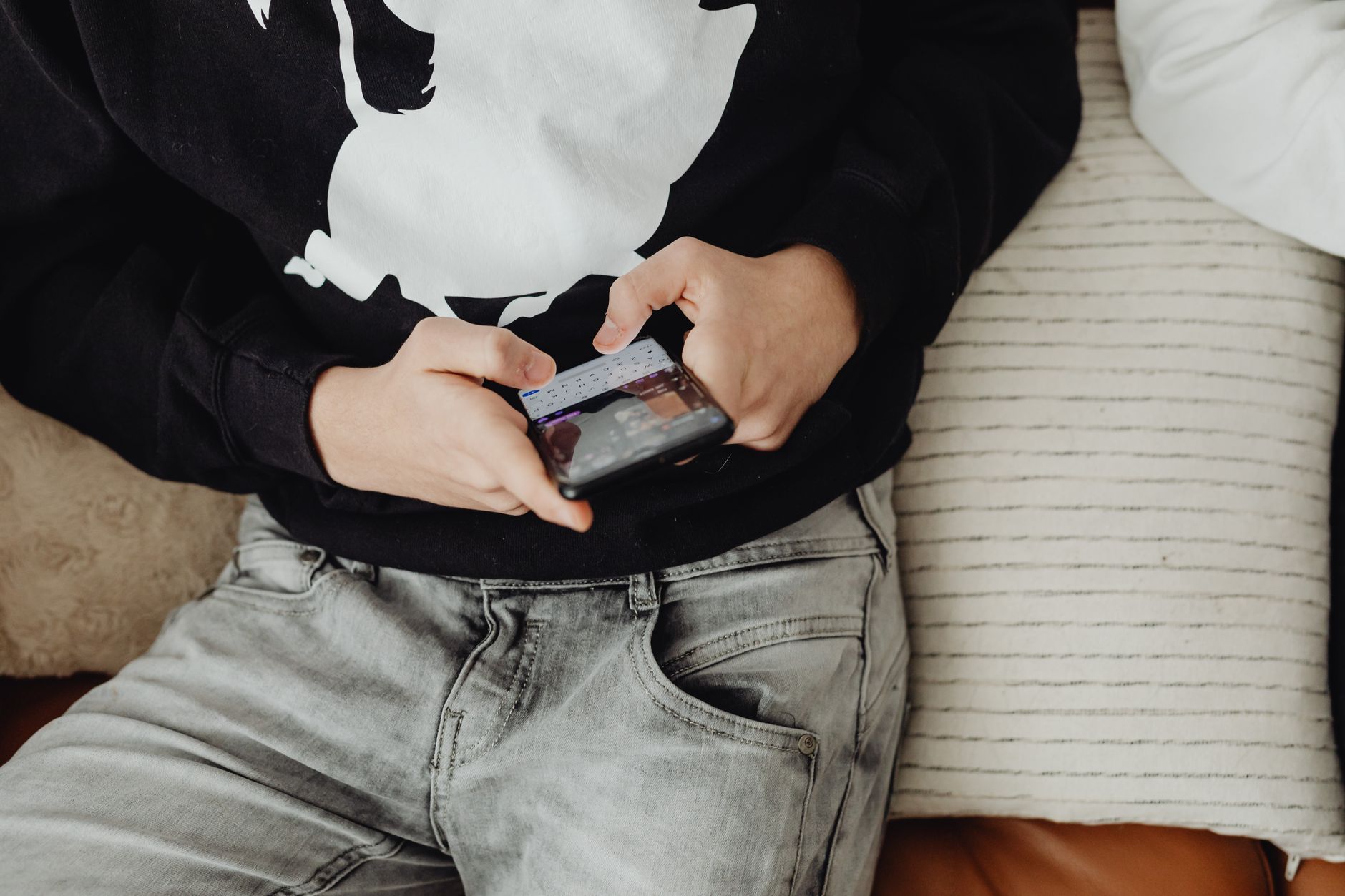 Close-up of a teenager sitting and using a smartphone on a comfortable sofa.