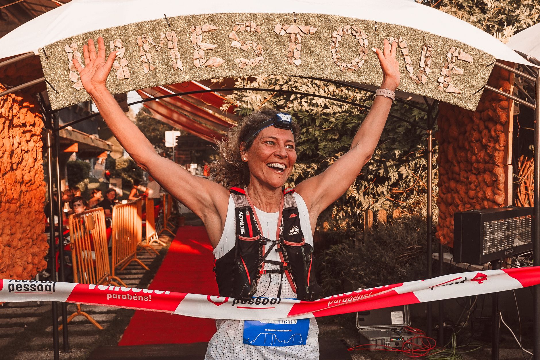 A joyful female marathon runner crosses the finish line with arms raised in victory.
