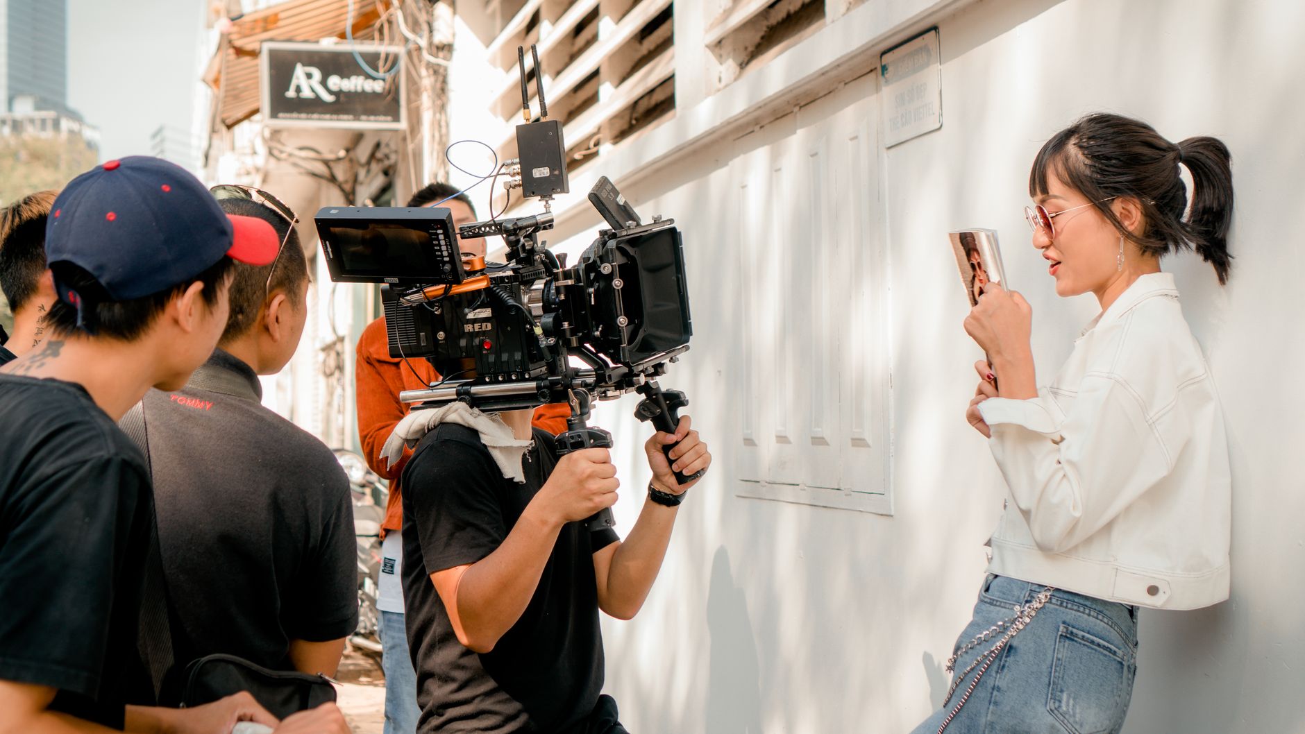 Film crew shooting a scene with professional video camera and actress outdoors on a sunny day.